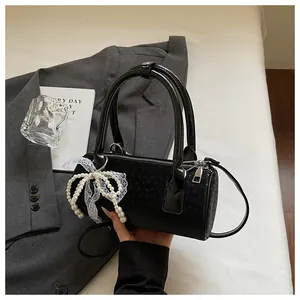 Close-up of black cylindrical handbag with pearl bow charm and lace detail
