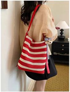 Detailed view of red and white striped knit bucket bag with shoulder strap and cute bear charm.