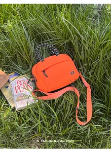 Vibrant orange outdoor crossbody bag placed in lush green grass with lifestyle props.