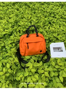 Vibrant orange hiking crossbody bag with rope handles on green foliage background.