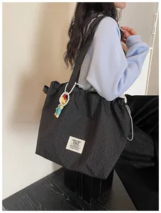 Close-up view of a black plaid canvas tote bag featuring a white logo label and cute charm
