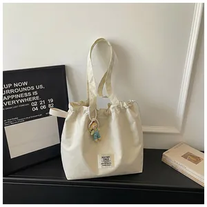 Casual cream canvas tote bag featuring a cute doll charm pendant and brand label detail
