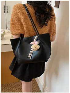 Large black faux leather tote bag with plush bear charm worn by a model in a cafe