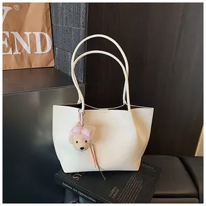 Cream white leather tote bag featuring a cute bear charm on an artistic book background.