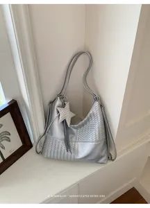 Vista detallada de un bolso tote tejido plateado con colgante de estrella y cinta a cuadros
