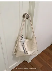 Bolso de hombro tejido minimalista crema colgado en una puerta con un colgante.