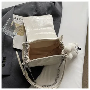 Detail shot of a chic cream white shoulder bag with chain strap and cute bear charm.