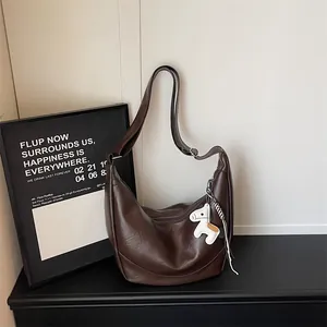 Detail view of a brown leather hobo dumpling shoulder bag with cute horse charm and slouchy design.