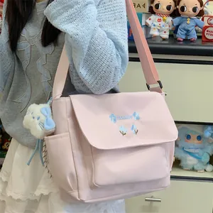 Pink canvas crossbody messenger bag with blue floral embroidery and adorable plush charm.