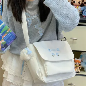 Casual white canvas messenger bag featuring blue floral embroidery and a cute plush pendant.