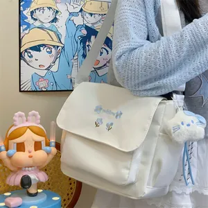 Detailed view of white canvas messenger shoulder bag with cute blue flower embroidery and charm.