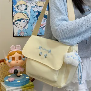 Detail view of cute canvas shoulder bag with floral embroidery and adorable plush keychain pendant.