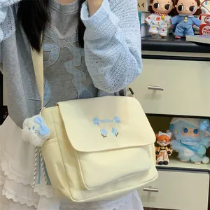 Canvas crossbody bag detail showing blue floral embroidery and cute plush pendant charm.