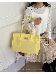 Detail shot of yellow jelly tote bag, large capacity handbag held by woman indoors.