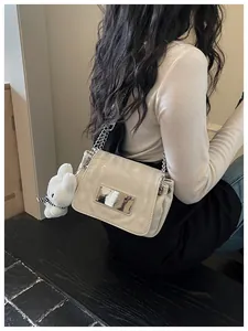 Close up view of white leather shoulder bag with chain strap and cute plush bunny charm.