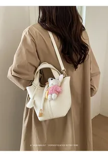 Detailed view of white leather bucket bag with cute plush charm and gold hardware retro style.