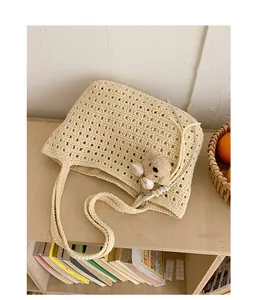 Gros plan d'un sac hobo en crochet crème avec motif tricot ajouré et breloque ours.