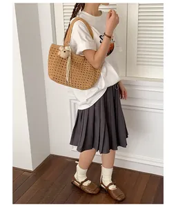 Modèle portant un sac bandoulière en paille tressé avec un charm d'ours pour les vacances.