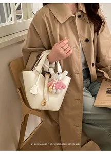 Detailed view of white bucket handbag with cute knit pendant and lock hardware chic style.
