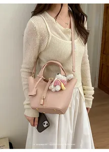 Chic pink leather bucket bag with top handle, crossbody strap and cute plush pendant.