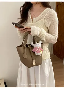 Detail view of stylish brown leather bucket handbag with metal lock and cute bear pendant.