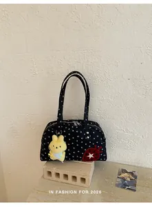 Détail de sac à main à pois chic avec pendentif lapin en peluche jaune et patch fraise rouge.
