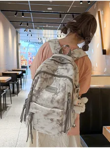 Close-up detail showing a tie-dye school backpack worn by a model in a modern cafe setting