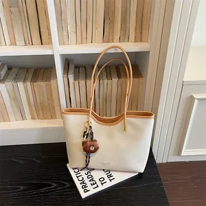 Detail view of the beige tote shoulder bag showcasing brown handles and cute bear charm.
