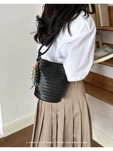 Detail view of a black woven bucket bag worn by a model, featuring stylish beaded charms.