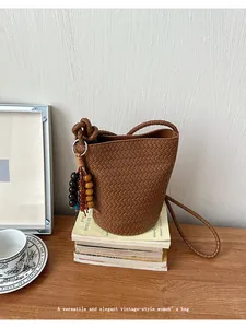 Brown woven bucket bag with stylish bead charm, retro shoulder crossbody design for summer.