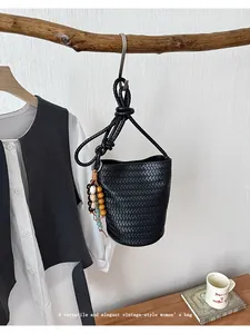Detail shot of black woven bucket bag with intricate leather texture and beaded charm pendant.
