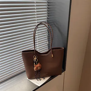 Detailed view of a stylish brown leather tote bag with delicate handles and cute bear pendant.