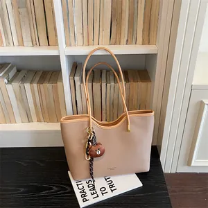 Detailed view of large capacity beige PU leather tote bag with cute bear charm and books.