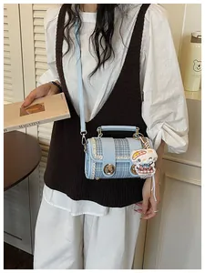 Close-up detail of light blue tweed boston shoulder bag with cute plush pendant and metal lock.