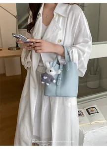 Minimalist light blue leather bucket bag with a cute rabbit charm shown on model