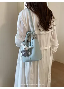 Close-up detail of light blue leather bucket bag with cute plush charms and shoulder strap.