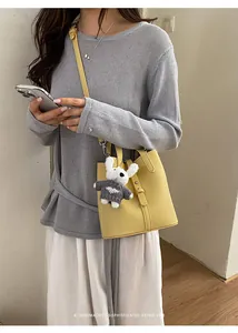 Yellow leather bucket bag detail shot with cute knit rabbit pendant, stylish and chic.
