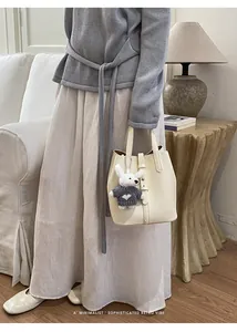 Minimalist PU leather bucket bag with cute plush keychain and stylish belt detail for women.