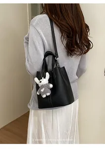 Black leather bucket bag featuring top handles, shoulder strap, and a cute white bear charm.