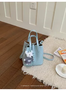 Detailed view of light blue pebbled leather bucket bag with a cute white bear charm
