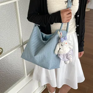 Vue détaillée du sac porté épaule en cuir tissé bleu clair avec joli porte-clés en peluche.