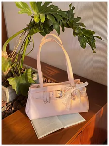 Détail de sac porté épaule rose avec boucle élégante et pendentif nœud perlé.
