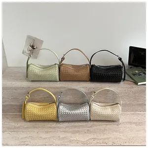 Detailed view of multiple woven cylinder handbags in various colors arranged neatly on a stone step.