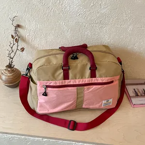 Color-blocked travel duffel bag detail, featuring durable pink pocket and red handles.