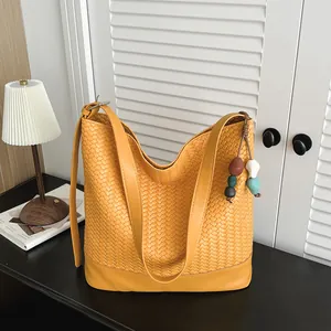 Detailed view of stylish yellow woven shoulder bucket bag with smooth base and bead charm decor.