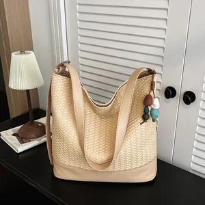 Beige woven bucket bag detail view, stylish shoulder bag texture and charm accessory.