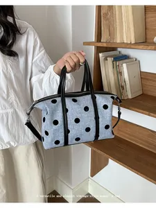 Bolso grande de lona azul con lunares negros sostenido cerca de una estantería
