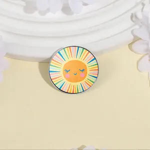 Fröhliche kreisförmige Metallbrosche mit buntem Sonnendesign auf cremefarbenem Grund.