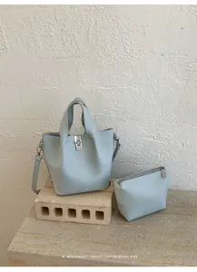 Elegante lichtblauwe bucket bag set met bijpassende pouch op een stenen voet gepresenteerd.