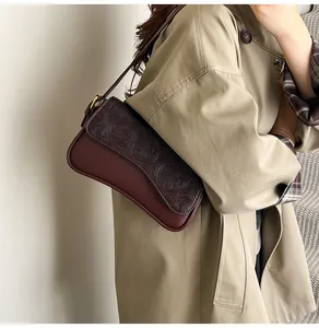 Detail shot of the elegant burgundy embossed shoulder bag worn with a stylish trench coat.